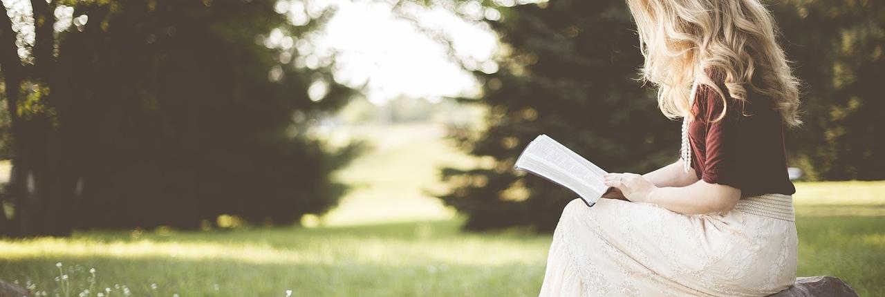 Bambina che legge un libro in un parco.