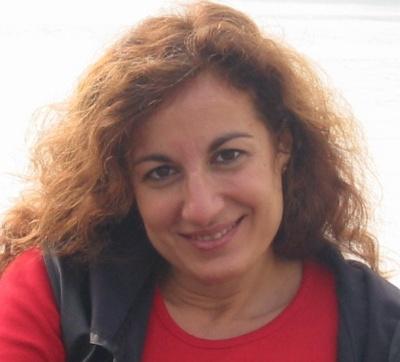 Una donna coi capelli lunghi sulla trentina, sorridente e con vestiti sportivi.