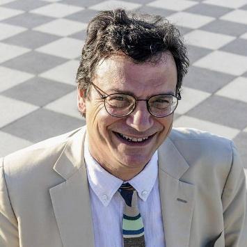 Un uomo giovane, vestito elegante, sulla quarantina che porta gli occhiali e sorride.